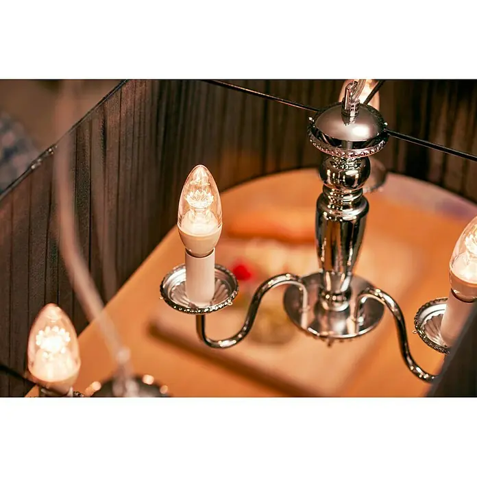 Philips Bombilla LED Vela - E14, Intensidad regulable, Blanco cálido, 470 lm, 6 W - Primer plano de un elegante candelabro de cromo con bombillas LED que emiten una luz cálida y acogedora. Iluminación elegante para cualquier hogar.