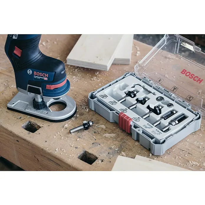 Bosch Fräser-Set Trim&Edging - 6 -tlg., Durchmesser Schaft: 8 mm - Nahaufnahme eines Bosch-Oberfräsen-Sets mit einer Oberfräse und verschiedenen Fräsern auf einer Werkbank, ideal für Holzarbeiten.