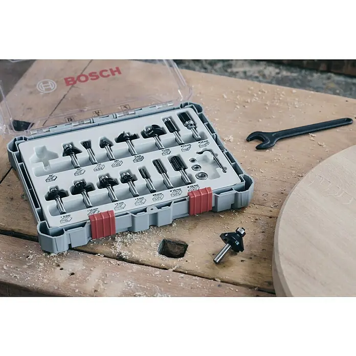 Bosch Fräser-Set Mixed - 15 -tlg., Durchmesser Schaft: 8 mm - Bosch-Fräser-Set in einem grauen Koffer mit rotem Verschluss auf einem Holztisch mit Sägespänen.