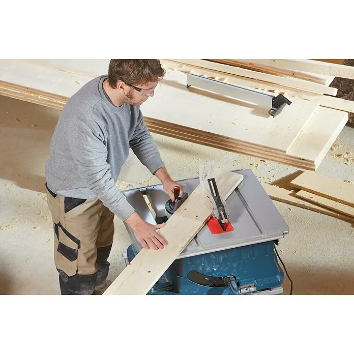 Bosch Professional Tischkreissäge GTS 635-216 - 1.600 W, Durchmesser Sägeblatt: 216 mm, Schnitttiefe bei 90 °: 70 mm, Ohne Untergestell - Ein Mann benutzt eine Tischkreissäge, um ein Holzbrett zu schneiden. Die Kreissäge ist blau und grau.