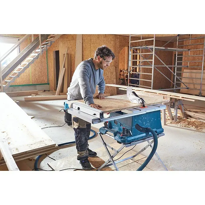 Bosch Professional Tischkreissäge GTS 635-216 - 1.600 W, Durchmesser Sägeblatt: 216 mm, Schnitttiefe bei 90 °: 70 mm, Ohne Untergestell - Ein Mann benutzt eine Bosch Tischkreissäge in einer Werkstatt, um ein Holzbrett zuzuschneiden. Die Säge steht auf einem stabilen Untergestell.