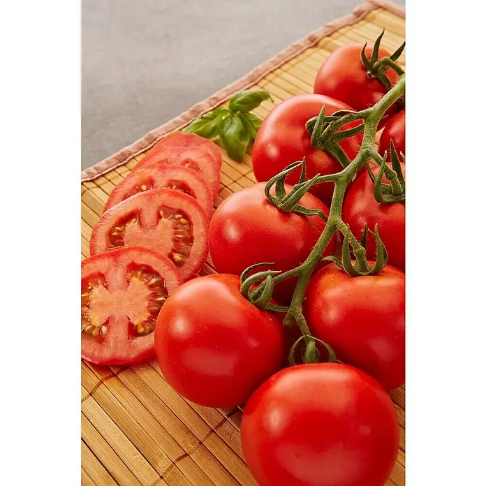 Strauchtomate veredelt - Solanum lycopersicum, 12 cm, Erntezeit: Juli - Frische Tomaten auf dem Holzbrett, teilweise in Scheiben geschnitten, mit einem grünen Basilikumblatt dekoriert. Perfekt für eine gesunde Mahlzeit.