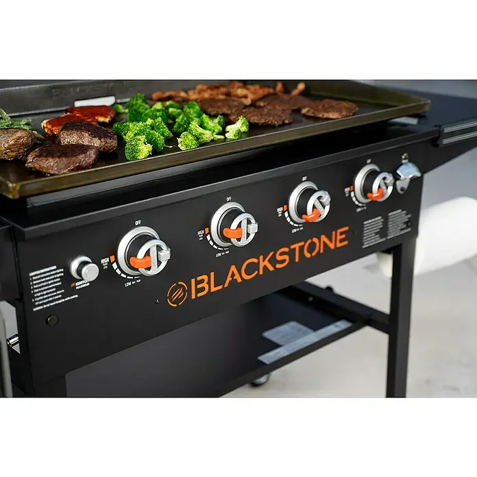 Blackstone Plancha-Grill 36" - Grillfläche (B x T): 91 x 55 cm, 17,5 kW, Anzahl Brenner: 4 Stk. - Blackstone Grill mit vier Reglern und einer Platte mit Fleisch, Brokkoli und Soße.