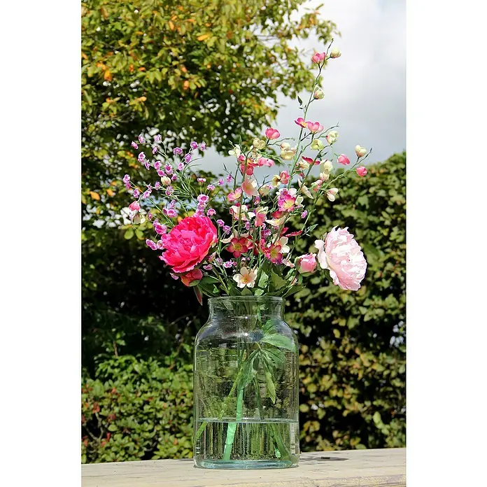 Vase Vienne - Ø x H: 21 x 35 cm, Glas, Transparent - Ein Glasgefäß mit einem bunten Blumenstrauß, darunter rosa Pfingstrosen, steht auf einem Tisch im Freien vor üppigem Grün.