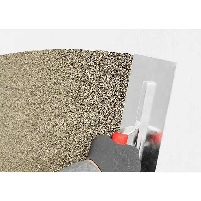 swingcolor Buntsteinputz - Korngröße: 2 - 3 mm, 20 kg, Nr. 50 - Nahaufnahme einer Person, die mit einer Kelle eine Wand mit Quarzputz verputzt. Die Textur und die Handwerkskunst stehen im Fokus.