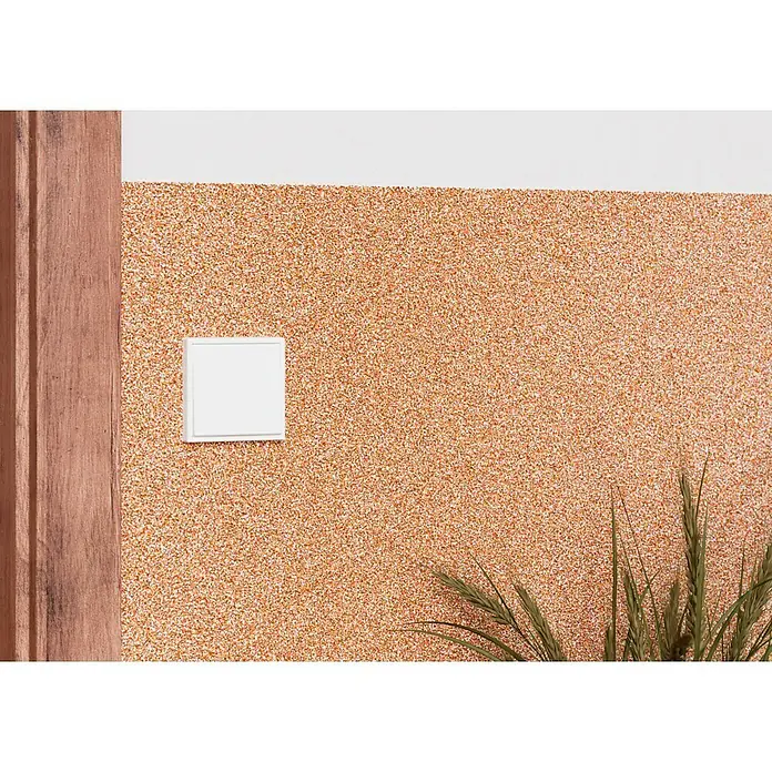 Probau WDVS-Buntsteinputz - Weiß/Orange/Rot, 25 kg - Eine Nahaufnahme einer weißen quadratischen Steckdose an einer Wand mit orangefarbenem Spritzputz, neben einem Holzrahmen.