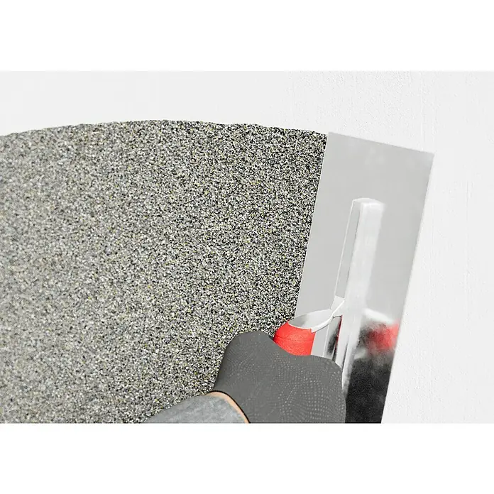 swingcolor Buntsteinputz - Korngröße: 2 - 3 mm, 20 kg, Nr. 51 - Ein Arbeiter glättet mit einer Glättkelle eine Wand mit dekorativem Edelputz, um eine gleichmäßige Textur zu erzielen.