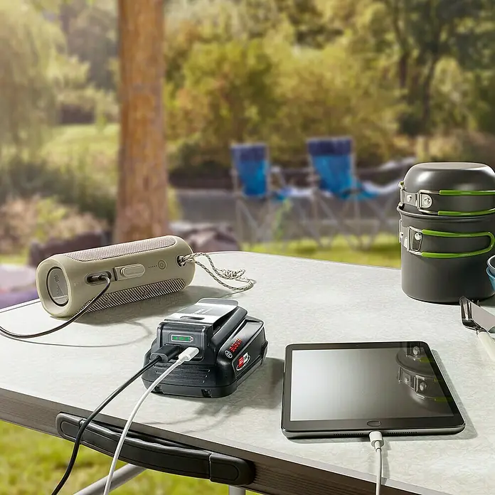 Bosch USB-Adapter Universal USB 18V-45 - Passend für: Power for All 18V Akkus - Lautsprecher, Akku und Tablet werden auf einem Campingtisch im Freien aufgeladen. Ein tragbares Kraftwerk versorgt alle Geräte mit Strom.