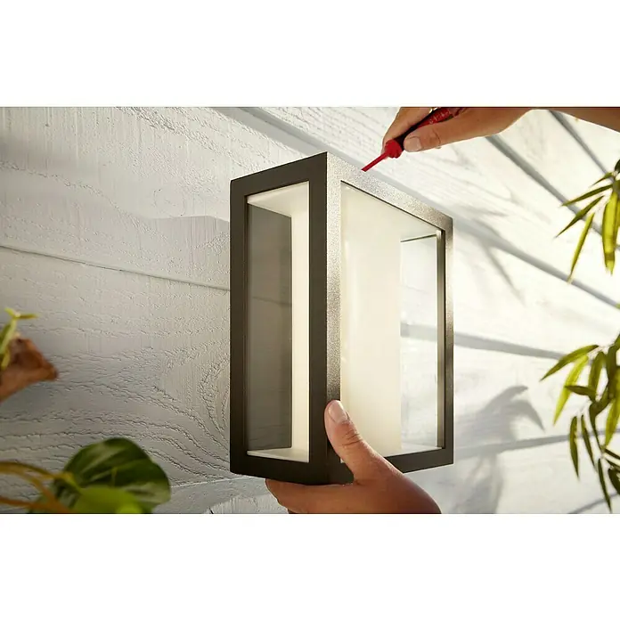 Philips Hue LED-Außenwandleuchte Impress - 8 W, 11,7 x 19 x 24 cm, Schwarz, IP44 - Nahaufnahme einer modernen Außenwandleuchte, die an einer Fassade befestigt wird, während eine Person eine Schraube festzieht.