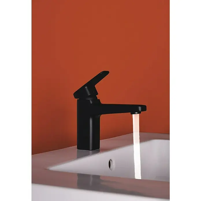 Ideal Standard Ceraplan Waschtischarmatur H90 - Schwarz, Matt, Ohne Ablaufgarnitur - Eine Nahaufnahme eines modernen, schwarzen Wasserhahns mit fließendem Wasser vor einem orangefarbenen Hintergrund.
