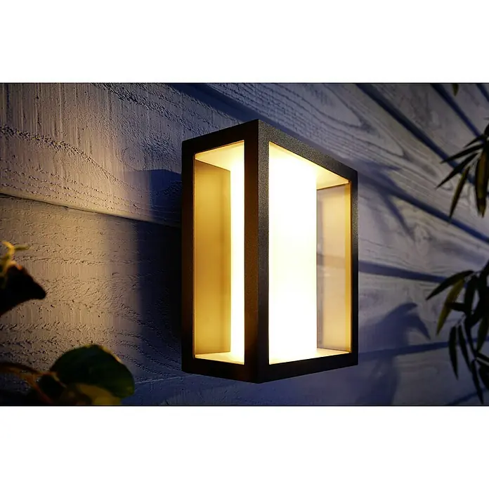 Philips Hue LED-Außenwandleuchte Impress - 8 W, 11,7 x 19 x 24 cm, Schwarz, IP44 - Nahaufnahme einer modernen, rechteckigen Außenwandleuchte mit warmer Beleuchtung, die an einer Holzwand befestigt ist.