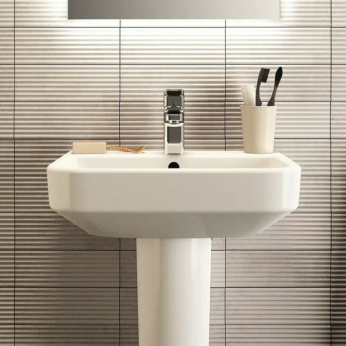 Ideal Standard i.life S Waschtisch50 x 38 cm, Ohne Spezialglasur, Hahnloch: Mitte, Mit Überlauf, Weiß - Nahaufnahme eines Waschbeckens mit Seife, Zahnbürsten und einem glänzenden Wasserhahn vor einem Hintergrund aus strukturierten Fliesen.