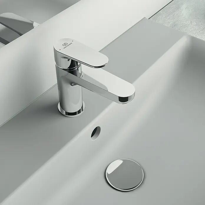 Ideal Standard Cerafine O Waschtischarmatur H80 - Chrom, Glänzend, Ohne Ablaufgarnitur - Nahaufnahme eines glänzenden, modernen Ideal Standard Waschtischhahns auf einem grauen Waschbecken, der Eleganz und Funktionalität vereint.