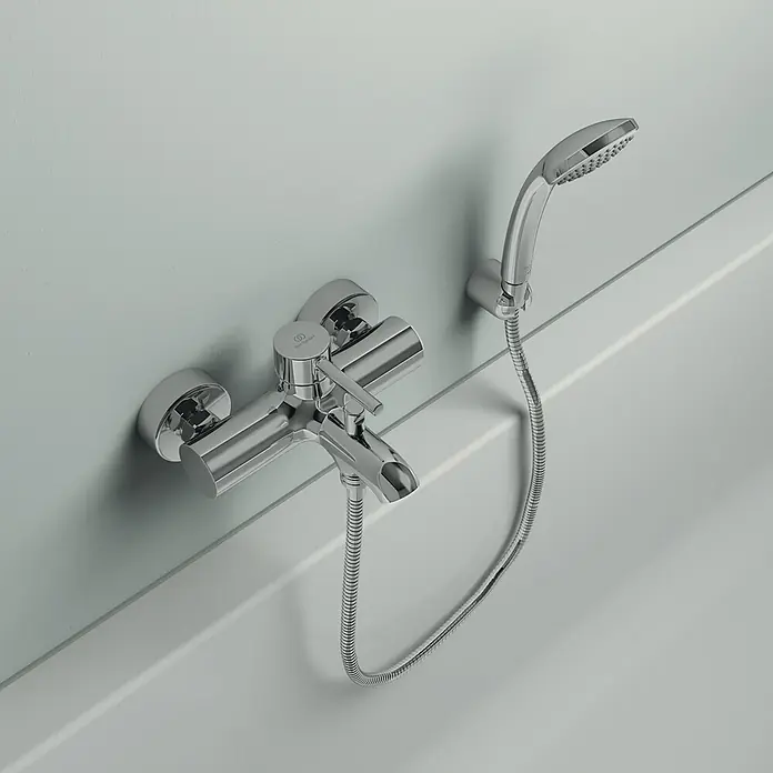 Ideal Standard Ceraline BadewannenarmaturChrom, Glänzend - Nahaufnahme einer glänzenden Chrom-Badewannenarmatur mit Brausegarnitur, die an einer hellgrauen Wand montiert ist.