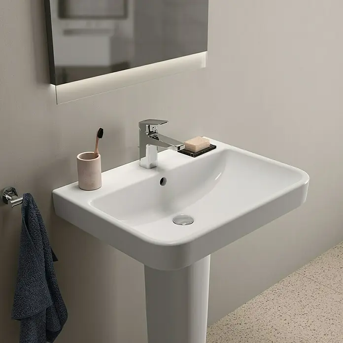 Ideal Standard i.life B Waschtisch - 65 x 48 cm, Ohne Spezialglasur, Hahnloch: Mitte, Mit Überlauf, Weiß - Nahaufnahme eines stilvollen, weißen Waschbeckens mit Armatur, Seife und einem Becher mit Zahnbürste im modernen Badezimmer.