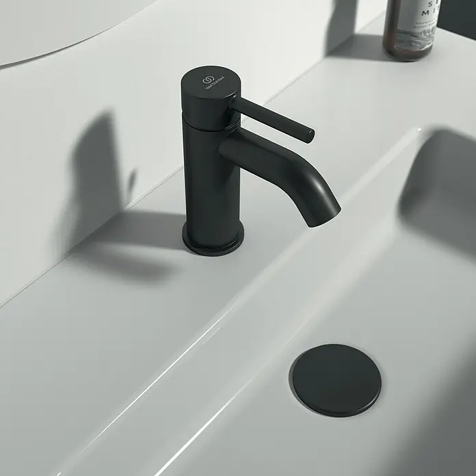 Ideal Standard Ceraline Waschtischarmatur - Schwarz, Matt, Mit Ablaufgarnitur - Nahaufnahme eines modernen, schwarzen Wasserhahns auf einem weißen Waschbecken, der ein stilvolles Badezimmerdesign betont.
