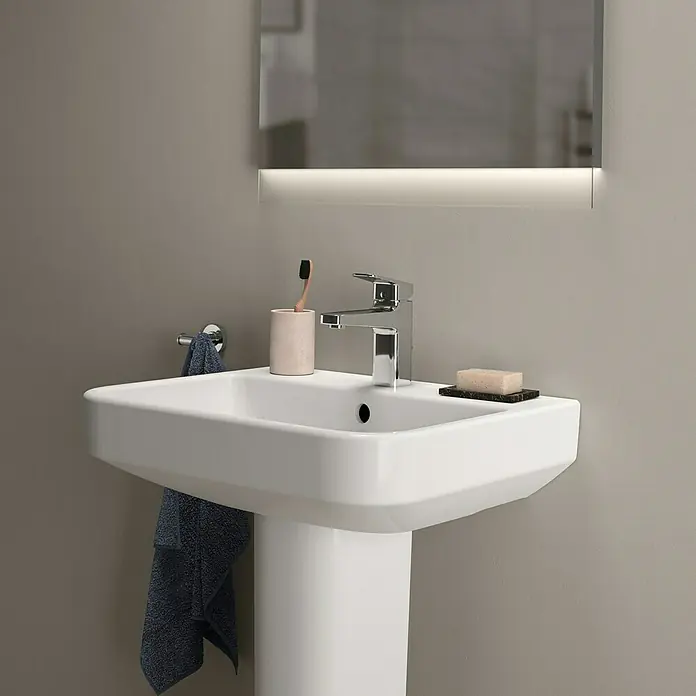 Ideal Standard i.life B Waschtisch - 55 x 48 cm, Ohne Spezialglasur, Hahnloch: Mitte, Mit Überlauf, Weiß - Das Bild zeigt ein modernes Waschbecken mit Armatur, Seife und Zahnbürste vor einem Spiegel in einem Badezimmer.