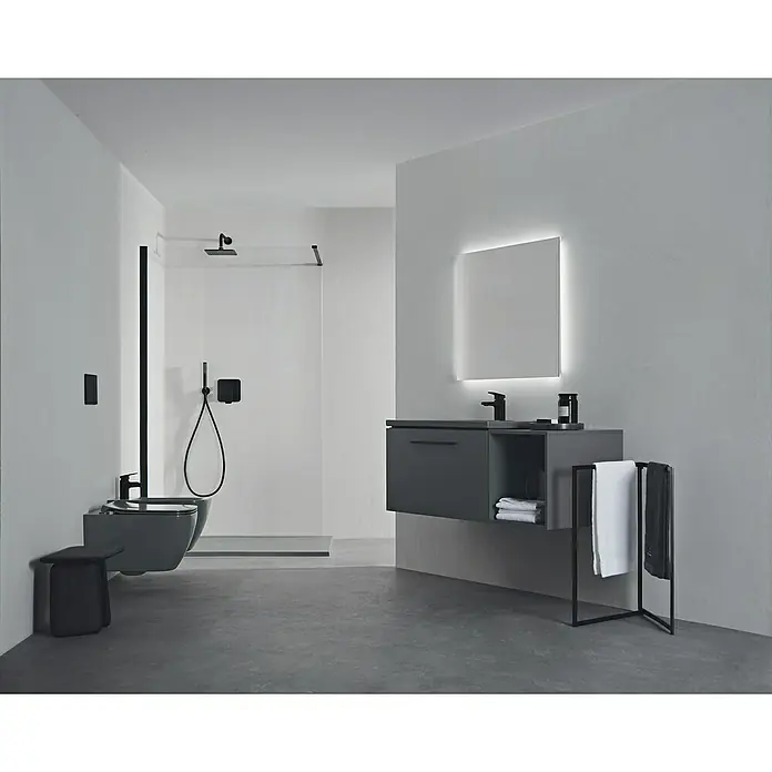 Ideal Standard Ceraplan Waschtischarmatur H75 - Schwarz, Matt - Ein modernes Badezimmer mit einem schwebenden Waschtisch in Grau, einem beleuchteten Spiegel und einer ebenerdigen Dusche mit schwarzen Armaturen.