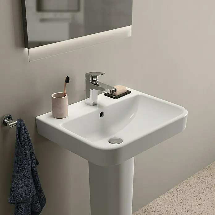 Ideal Standard i.life B Waschtisch - 55 x 48 cm, Ohne Spezialglasur, Hahnloch: Mitte, Mit Überlauf, Weiß - Nahaufnahme eines modernen Waschbeckens mit Armatur, Seife und Zahnbürste in einem stilvollen Badezimmer.