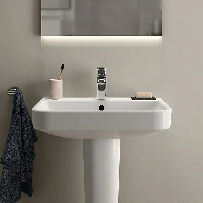 Ideal Standard i.life B Waschtisch60 x 48 cm, Ohne Spezialglasur, Hahnloch: Mitte, Mit Überlauf, Weiß - Nahaufnahme eines modernen Waschbeckens mit Armatur, Seife und Handtuch, hervorgehoben durch ein helles Licht.