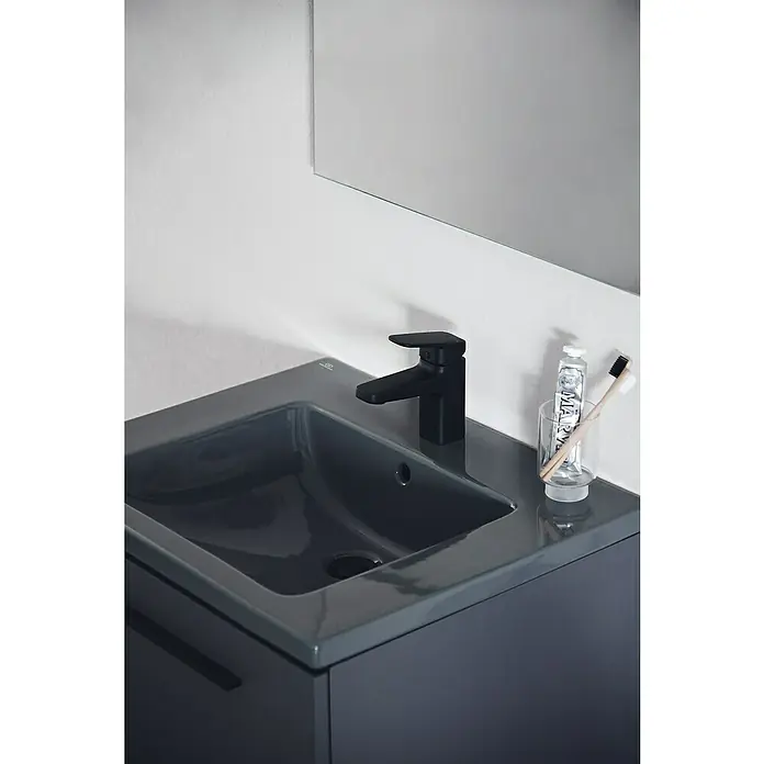Ideal Standard Ceraplan Waschtischarmatur H75 - Schwarz, Matt - Nahaufnahme eines modernen Badezimmers mit einem eleganten, grauen Waschbecken, einem schwarzen Wasserhahn und einer Zahnbürste neben einer Tube Zahnpasta.