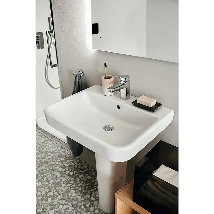 Ideal Standard i.life B Waschtisch - 60 x 48 cm, Ohne Spezialglasur, Hahnloch: Mitte, Mit Überlauf, Weiß - Ein Waschbecken mit Armatur, Zahnputzbecher, Seife und Handtuch in einem modernen Badezimmer mit Terrazzoboden.