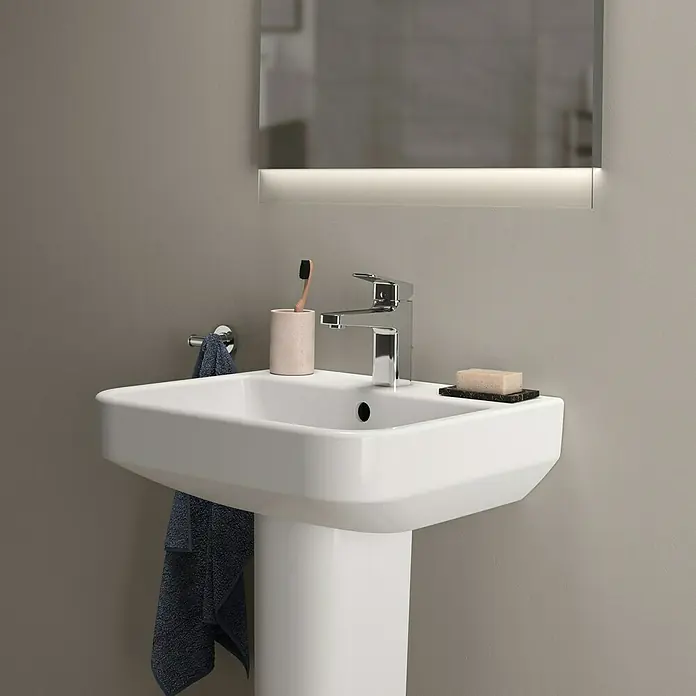 Ideal Standard i.life B Waschtisch - 50 x 44 cm, Ohne Spezialglasur, Hahnloch: Mitte, Mit Überlauf, Weiß - Nahaufnahme eines weißen Waschbeckens mit Armatur, Seife, Zahnbürste und Handtuch in einem modernen Badezimmer.