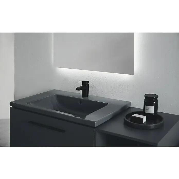 Ideal Standard Ceraplan Waschtischarmatur H75Schwarz, Matt - Moderne Badezimmerarmatur mit Waschbecken und Ablagefläche für Seife und Lotion, beleuchtet durch einen Spiegel.