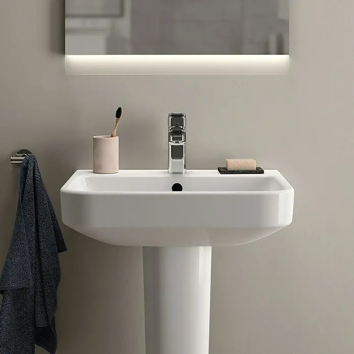 Ideal Standard i.life B Waschtisch55 x 48 cm, Ohne Spezialglasur, Hahnloch: Mitte, Mit Überlauf, Weiß - Ein Waschbecken mit Handtuchhalter, Armatur, Seife und Zahnbürste. Das Waschbecken ist weiß und hat eine moderne Form.