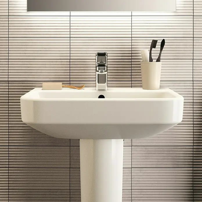 Ideal Standard i.life S Waschtisch - 55 x 38 cm, Ohne Spezialglasur, Hahnloch: Mitte, Mit Überlauf, Weiß - Elegantes Waschbecken mit Armatur, Seife, Zahnbürsten und Becher vor einem Hintergrund mit strukturierten Fliesen.