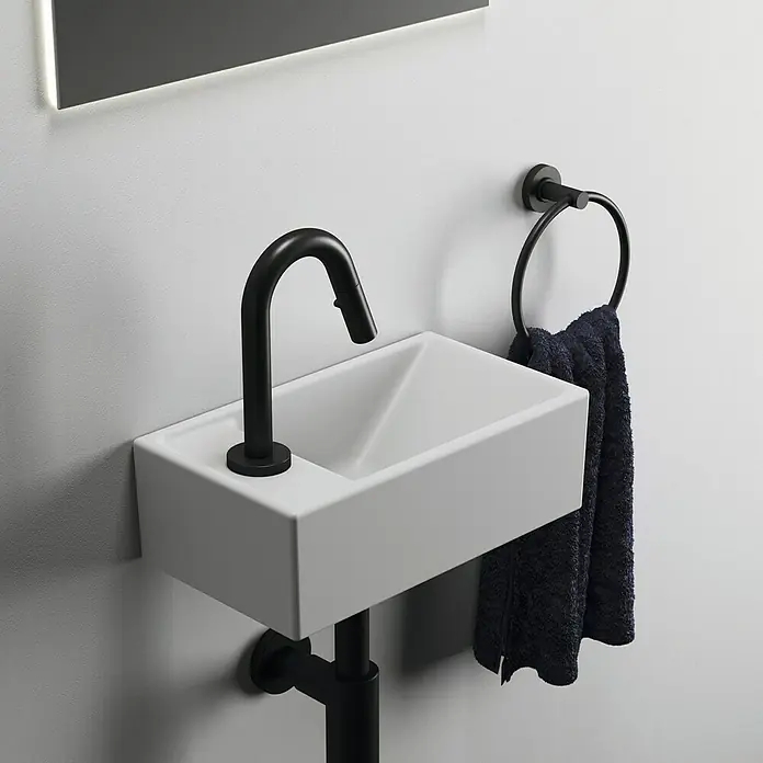 Ideal Standard Waschtisch-Siphon - 1 ¼″, Pulverbeschichtet, Schwarz - Nahaufnahme eines modernen Badezimmerwaschbeckens mit schwarzem Wasserhahn und Handtuchhalter an einer weißen Wand.
