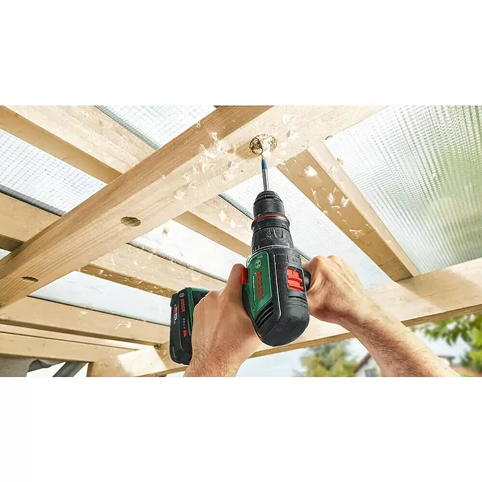 Bosch Power for All 18V Taladro atornillador de batería AdvancedDrill 18V-80 - 18 V, Sin batería, 78 Nm - Manos sostienen un taladro sin cable Bosch negro y verde, perforando una viga de madera con virutas.