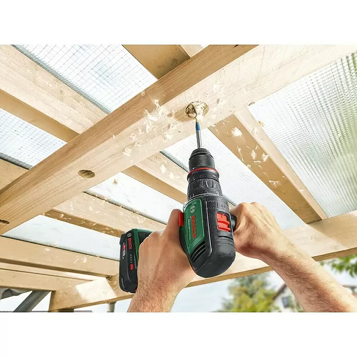 Bosch Power for All 18V Taladro atornillador de batería AdvancedDrill 18V-80 - 18 V, Sin batería, 78 Nm - Taladro inalámbrico Bosch verde y negro, sostenido por manos, taladrando activamente una viga de madera. Virutas de madera vuelan.