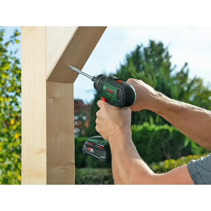 Bosch Power for All 18V Akku-Schlagbohrschrauber Advanced Impact 18V-80 QuickSnap - 18 V, Ohne Akku, 82 Nm, 3 Aufsätze - Eine Person schraubt mit einem grünen Bosch Akku-Bohrschrauber eine Schraube in ein Holzstück. Das Werkzeug ist kompakt und leistungsstark.