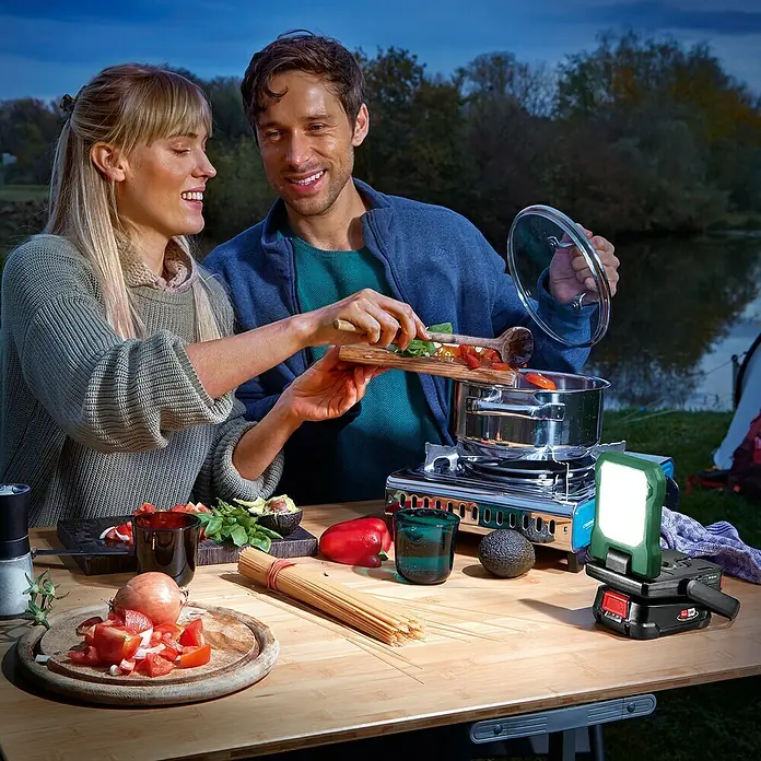 Bosch Power for All 18V Akku-Lampe Easy SpotLight 18V-400 - 18 V, Ohne Akku, 3 Helligkeitsstufen - Ein Paar kocht mit einem Campingkocher im Freien, beleuchtet von einer tragbaren Arbeitsleuchte.