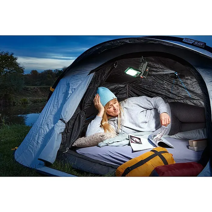 Bosch Power for All 18V Akku-Lampe Easy SpotLight 18V-400 - 18 V, Ohne Akku, 3 Helligkeitsstufen - Frau liest in einem 'Fresh Black'-Zelt mit einer hellen Zeltlaterne über sich, um das Campingerlebnis zu optimieren.