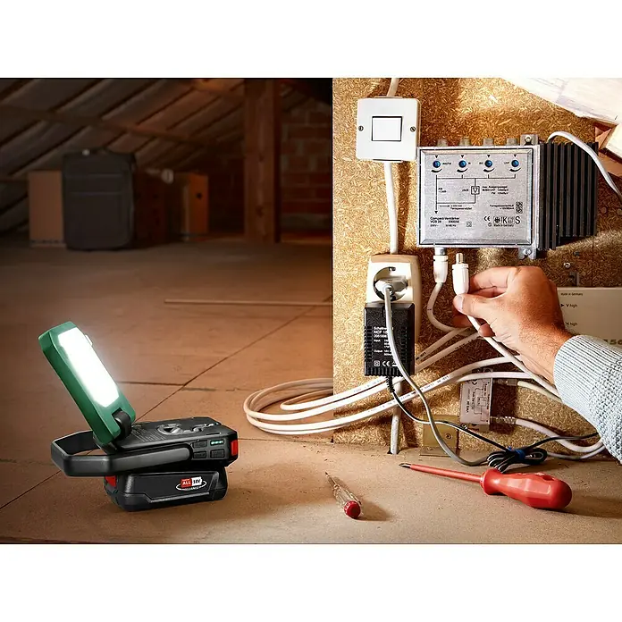 Bosch Power for All 18V Akku-Lampe Easy SpotLight 18V-400 - 18 V, Ohne Akku, 3 Helligkeitsstufen - Auf dem Dachboden steht eine akkubetriebene Arbeitsleuchte mit hell leuchtender LED, daneben Werkzeug und verschiedene elektronische Geräte.