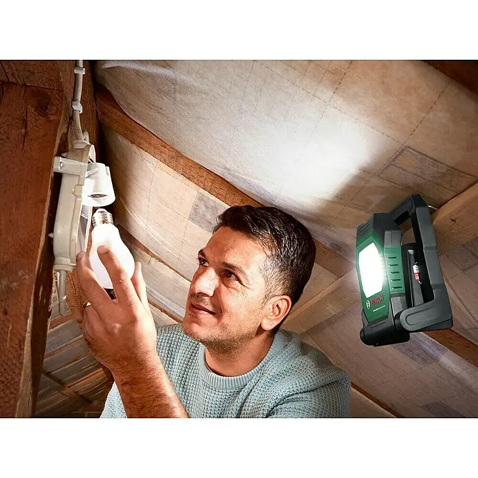 Bosch Power for All 18V Akku-Lampe UniversalWorkLight 18V-2100 - 18 V, Ohne Akku, 3 Helligkeitsstufen - Ein Mann wechselt eine Glühbirne, während eine Bosch Arbeitsleuchte für zusätzliches Licht sorgt.