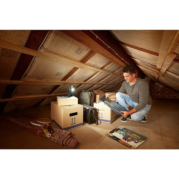 Bosch Power for All 18V Akku-Lampe UniversalWorkLight 18V-2100 - 18 V, Ohne Akku, 3 Helligkeitsstufen - Mann durchsucht Kartons auf einem Dachboden, eine Bosch-Arbeitsleuchte sorgt für gute Sicht, um alte Schallplatten zu finden.