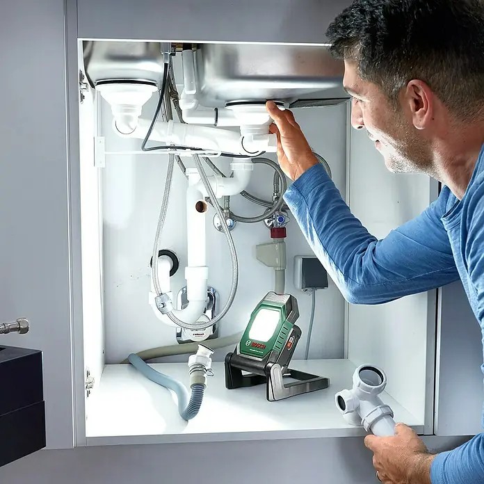 Bosch Power for All 18V Akku-Lampe UniversalWorkLight 18V-2100 - 18 V, Ohne Akku, 3 Helligkeitsstufen - Der Handwerker beleuchtet mit einer Bosch Lampe den Bereich unter der Spüle, um die Rohre zu reparieren.