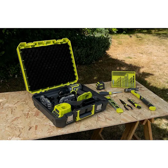 Ryobi ONE+ Akku-Bohrschrauber "Heimwerker-Set" RDD18-2C20TAH - 18 V, 2 Akkus, 2 Ah, 52 Nm - Ein Ryobi-Werkzeugset mit Akku-Bohrschrauber, Akkus, Ladegerät, Bohrern, Hammer, Schraubendreher, Maßband, Wasserwaage, Zange und Messer auf einem Holztisch.