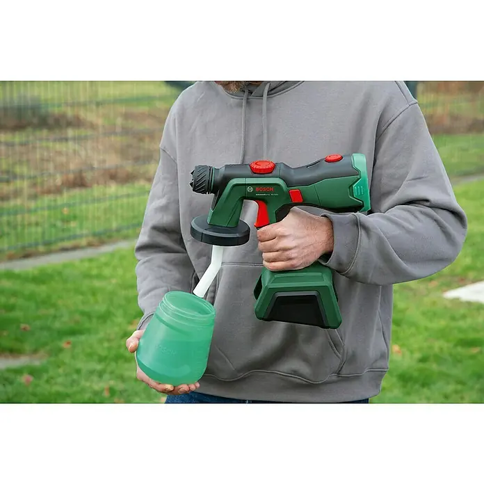 Bosch Power for All 18V Akku-Farbsprühsystem AdvancedSpray 18V-500 - 18 V, Ohne Akku, Max. Fördermenge: 500 l/h - Ein Mann hält eine Bosch Farbspritzpistole, Modell AdvancedSpray 18V-500, mit einem Behälter grüner Flüssigkeit in der Hand.
