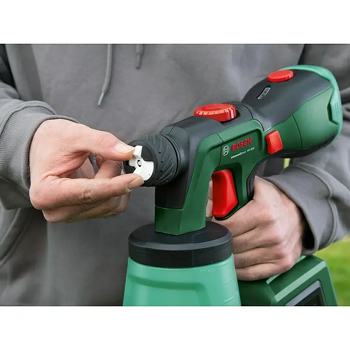 Bosch Power for All 18V Akku-Farbsprühsystem AdvancedSpray 18V-500 - 18 V, Ohne Akku, Max. Fördermenge: 500 l/h - Eine Person justiert die Düse einer grünen Bosch AdvancedSpray 18V-500 Farbspritzpistole mit roten Akzenten.