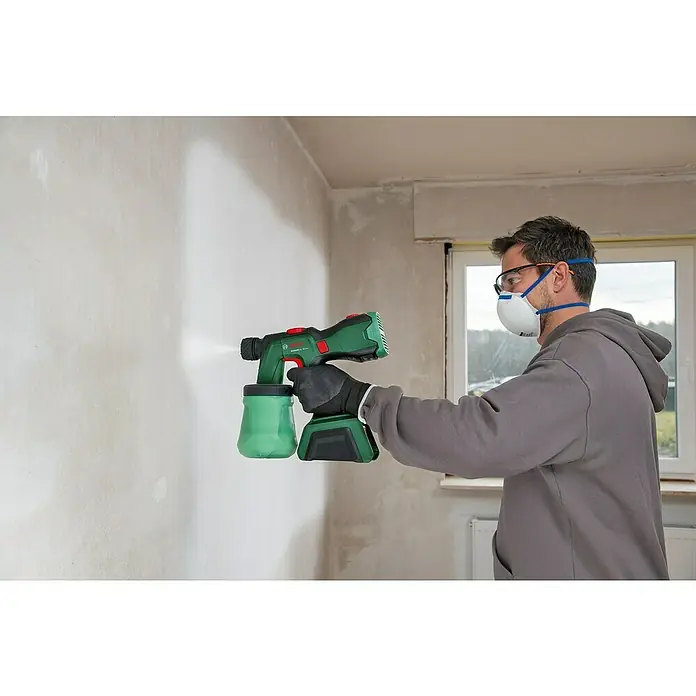 Bosch Power for All 18V Akku-Farbsprühsystem AdvancedSpray 18V-500 - 18 V, 1 Akku, 4 Ah, Max. Fördermenge: 0,5 l/min - Ein Mann sprüht mit einer Bosch Farbspritzpistole eine Wand. Die Spritzpistole ist grün und schwarz, der Mann trägt Schutzbrille und Maske.