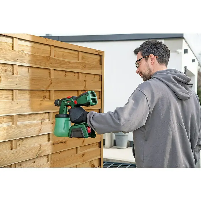 Bosch Power for All 18V Akku-Farbsprühsystem AdvancedSpray 18V-500 - 18 V, Ohne Akku, Max. Fördermenge: 500 l/h - Ein Mann sprüht mit einer Bosch Farbspritzpistole auf einen Holzzaun, der eine gleichmäßige Farbschicht erhält. Das Gerät ist kabellos und einfach zu bedienen.