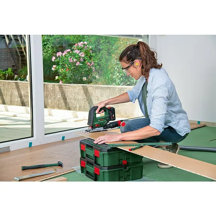 Bosch Power for All 18V Akku-Stichsäge Advanced Saw 18V-140 - 18 V, Ohne Akku, Leerlaufhubzahl: 3.000 /min - Eine Frau benutzt eine Bosch Stichsäge, um ein Stück Holz zu schneiden. Sie trägt Sicherheitsausrüstung, um sich vor Verletzungen zu schützen.