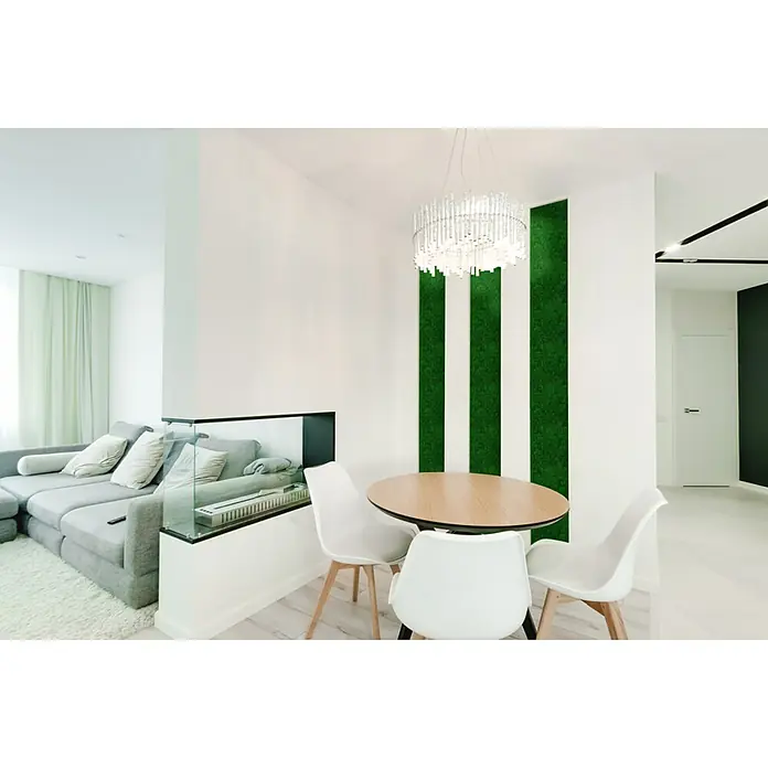 Jangal Wandpaneel Modular Wall Moos - Nature Green, 520 x 520 x 30 mm - Helles Interieur mit einem runden Holztisch, umgeben von weißen Stühlen, unter einer dekorativen Leuchte und vor einer grünen Wandgestaltung.
