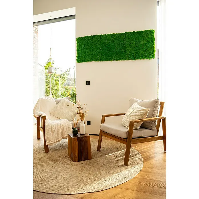 Jangal Wandpaneel Modular Wall Moos - Rich Green, 520 x 520 x 30 mm - Wohnzimmerbereich mit zwei Holzstühlen, einem runden Teppich und einem Couchtisch aus Holz, dekoriert mit einem grünen Wandpaneel.