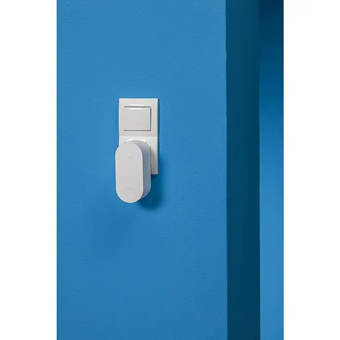 Abus Steuerzentrale BRIDGE ONE CFW3100W - Weiß, B x H: 55 x 52 mm - Steckdosen-Bewegungsmelder von ABUS an einer blauen Wand montiert.