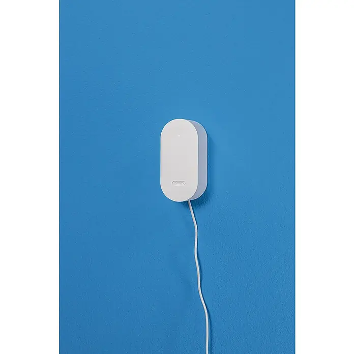 Abus Steuerzentrale BRIDGE ONE CFW3100W - Weiß, B x H: 55 x 52 mm - Nahaufnahme eines ABUS-Bewegungsmelders in Weiß, der an einer blauen Wand befestigt ist und ein Kabel hat.